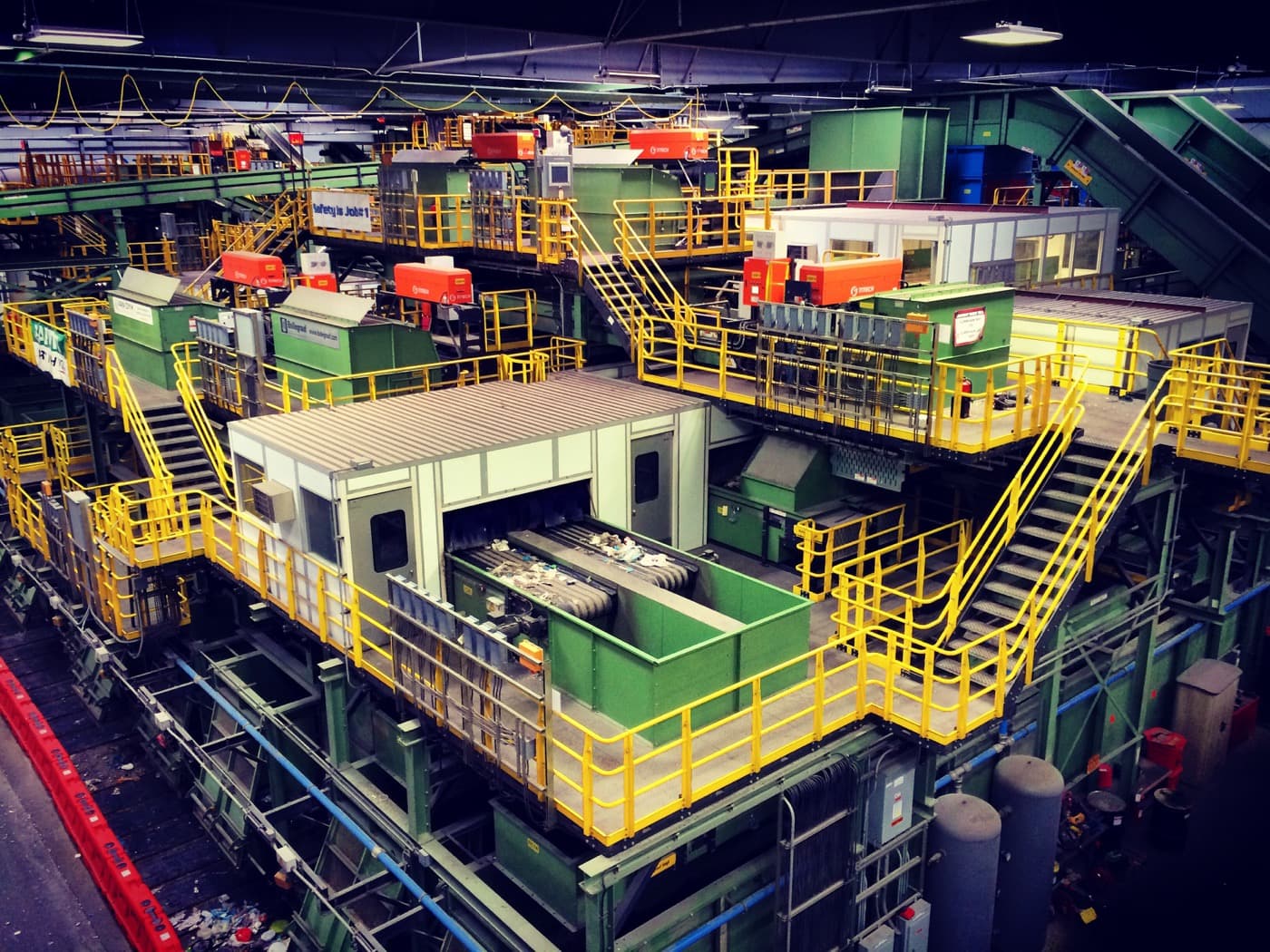 A high-angle view of an industrial material recovery facility with yellow safety rails and sorting equipment.